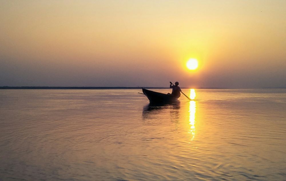 person with boat in brahmaputra river during sunset