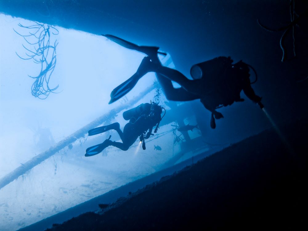 two scuba divers getting inside of a old ship