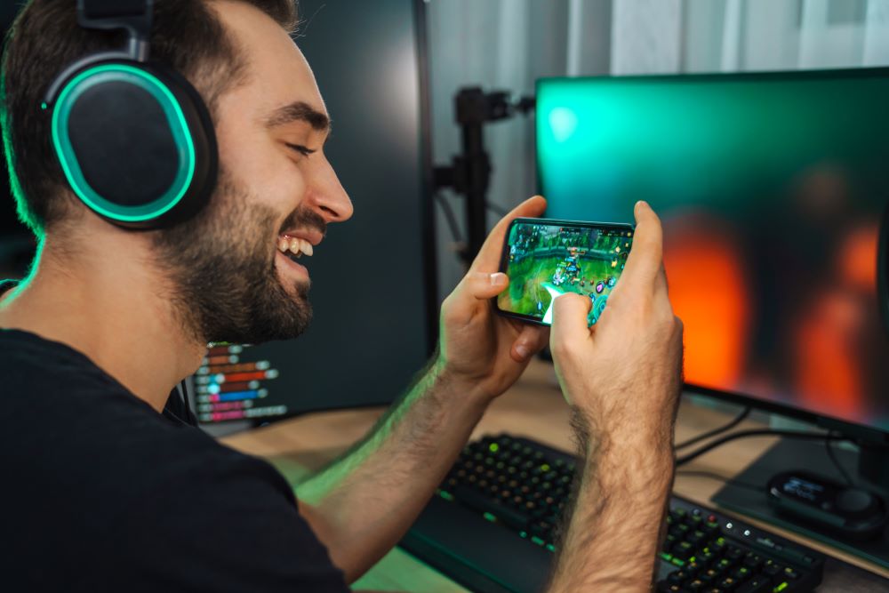 man playing game in mobile phone infront of computer