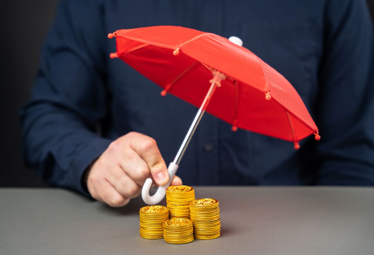 businessman holding umbrella over stack of coins